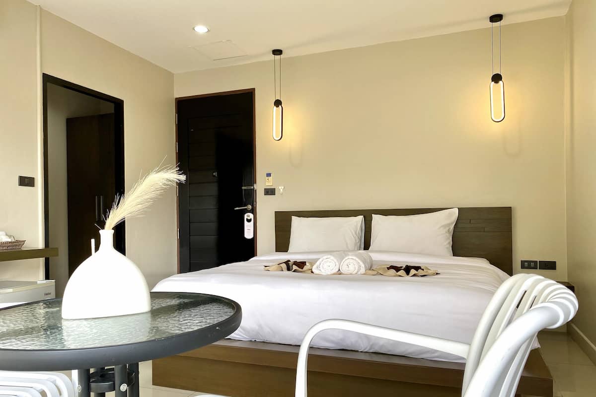 A hotel room with a neatly made bed, a round table with a glass top, and a white chair.