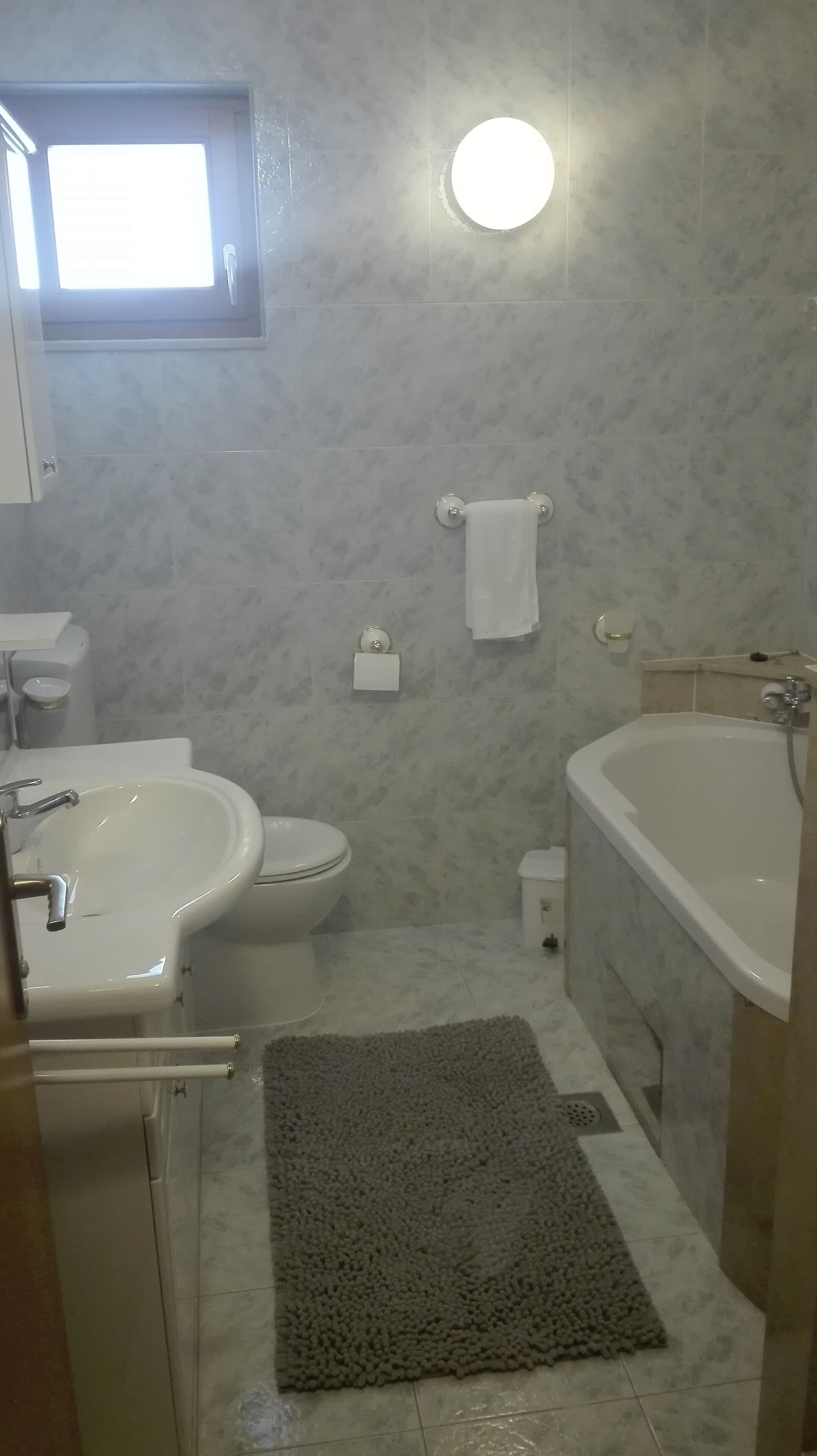 A bathroom with a sink, toilet, and bathtub. There is a towel rack with a towel hanging on it, and a small window above the toilet.