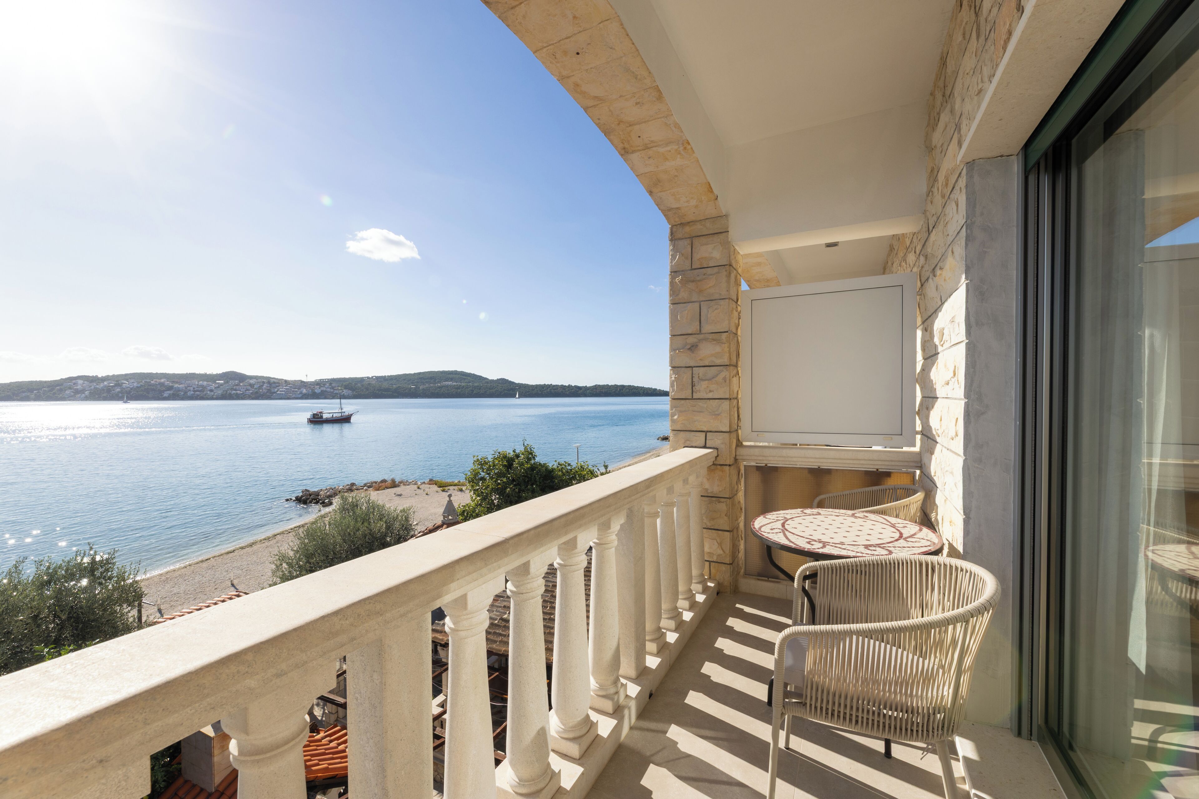 Un balcon avec vue sur la mer, une table avec des chaises et un mur en pierre.