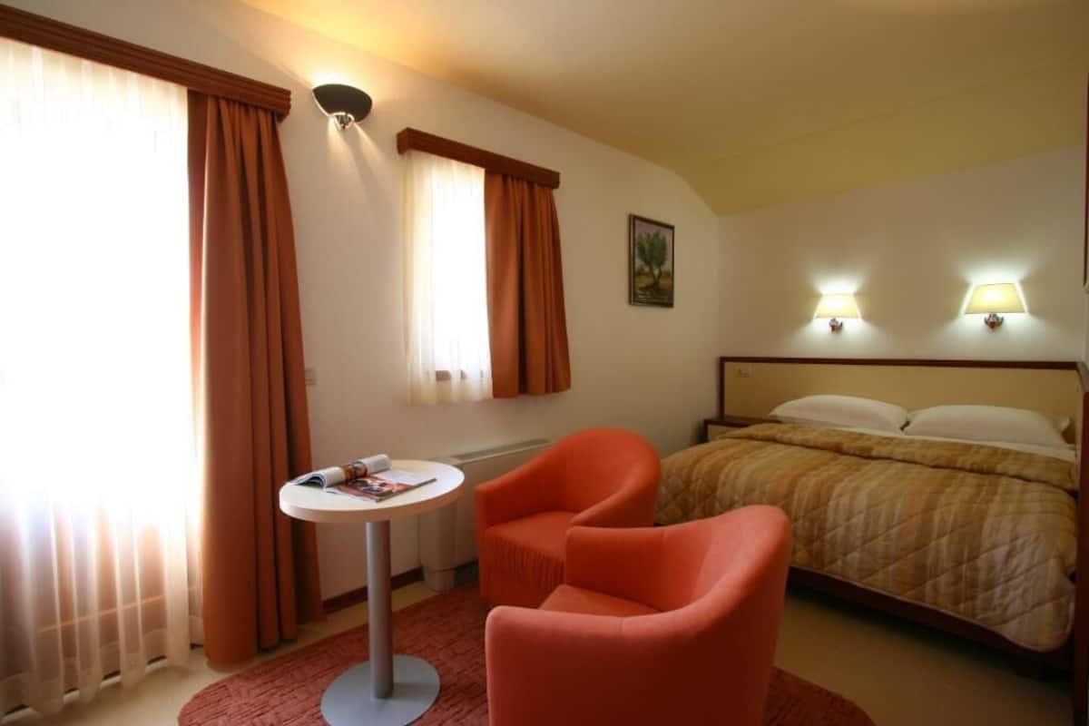 A hotel room with a bed, a round table, an orange chair, and two wall-mounted lamps.