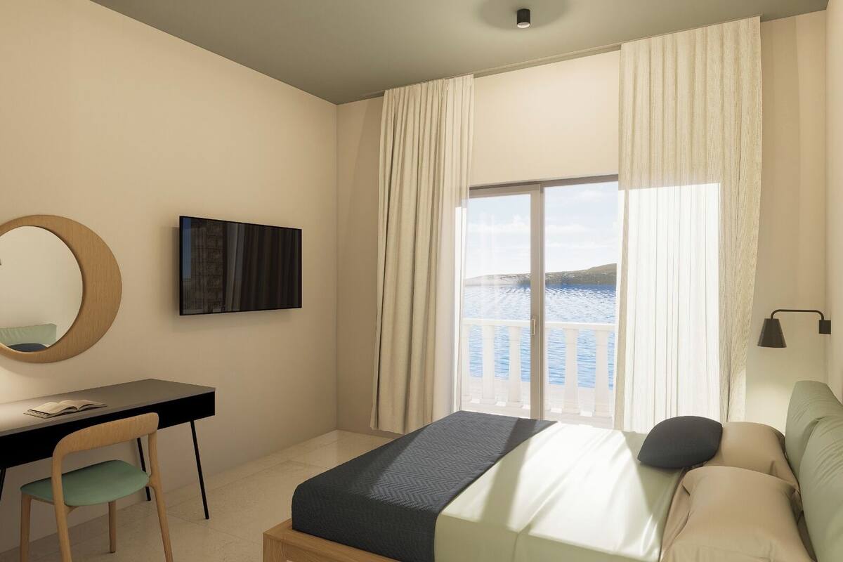 A hotel room with a bed, a desk, a chair, a TV, a window with curtains, and a view of the sea.