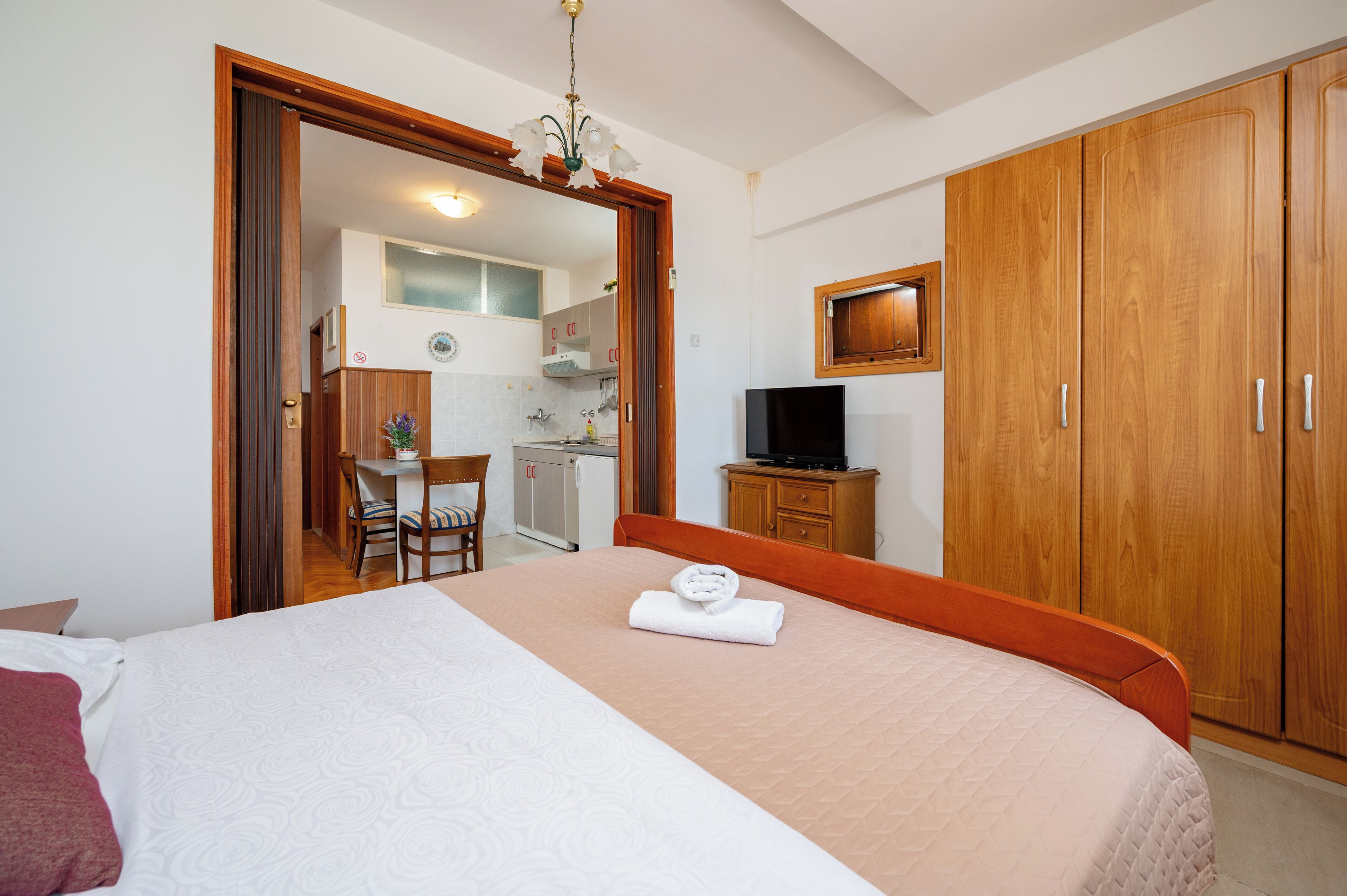 A hotel room with a bed, a desk, a chair, a television, and wooden wardrobes.