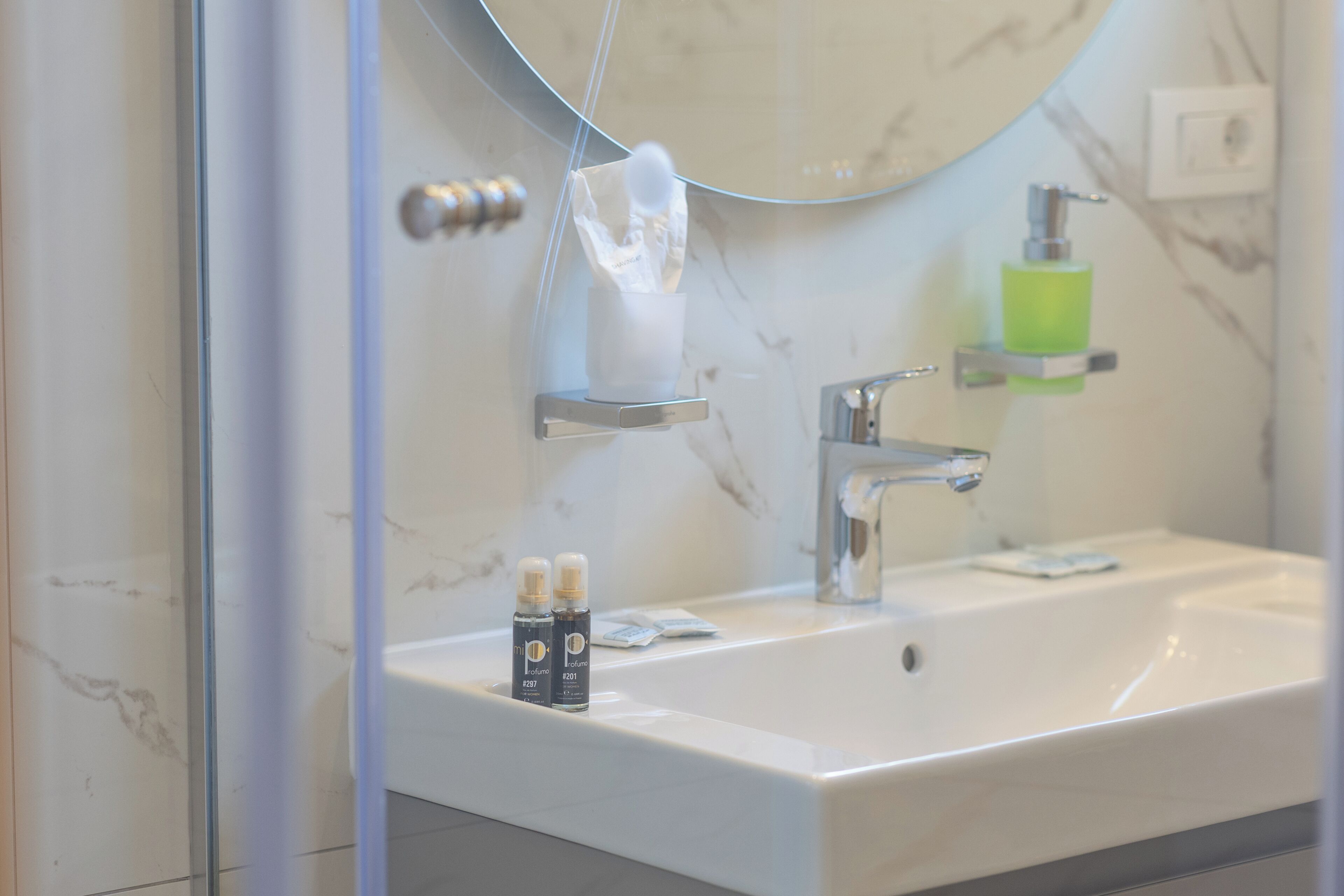 A bathroom with a white sink, a mirror, a glass shower enclosure, and a soap dispenser.