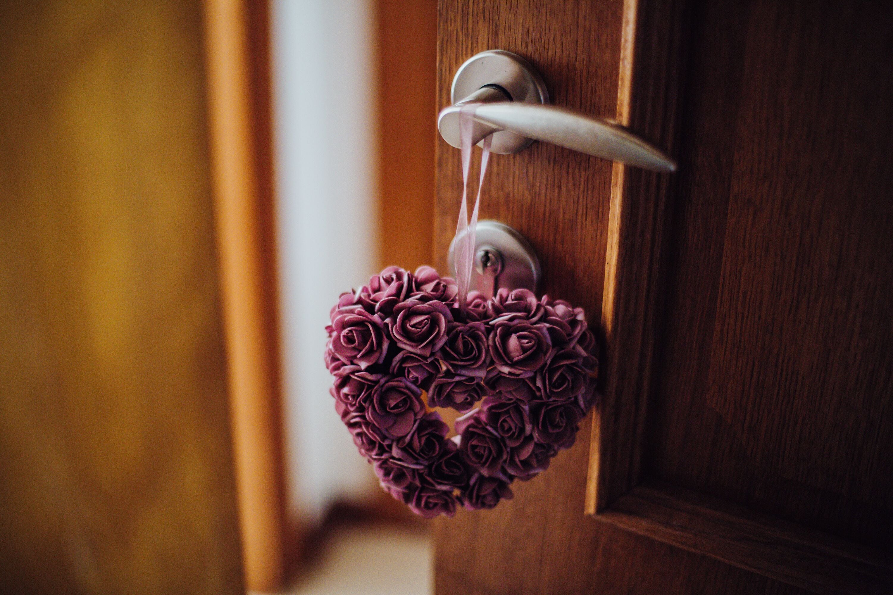 Uma porta com um enfeite em formato de coração com rosas roxas.