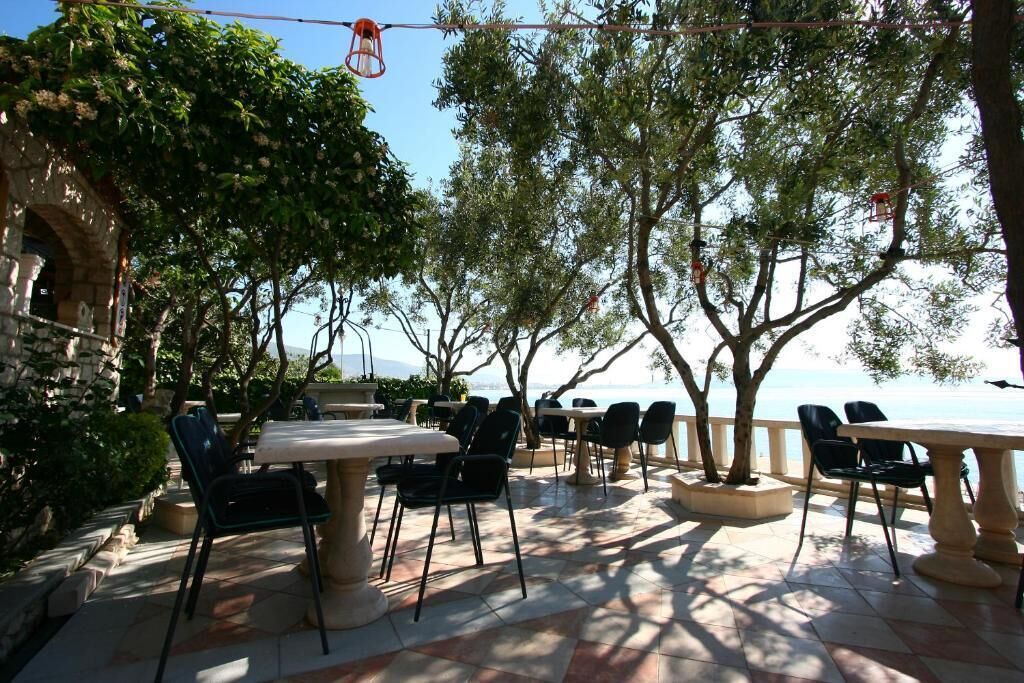 An outdoor patio with tables and chairs, surrounded by trees and overlooking a body of water.