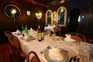 Comedor con una larga mesa dispuesta para una comida, que incluye una botella de vino, copas y cubiertos ordenados.
