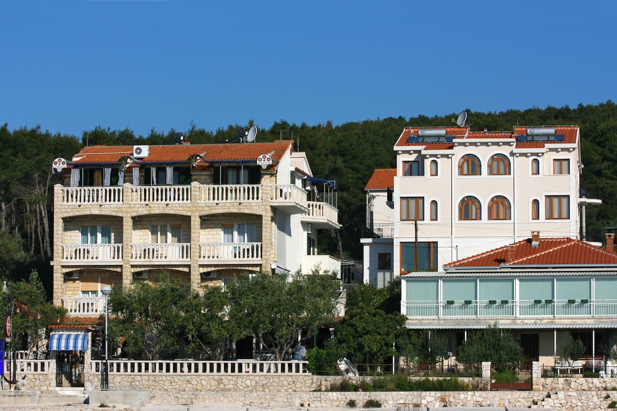 A multi-story building with balconies and a flat roof, surrounded by trees and a clear sky.