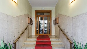 Un escalier en marbre, recouvert d’un tapis rouge, mène à une porte en bois dotée de panneaux de verre.