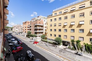 Une vue de rue avec des voitures garées, une voiture rouge au premier plan, et des immeubles à plusieurs étages dotés de balcons et de fenêtres.