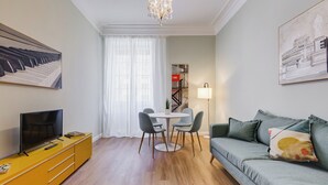 Un salon moderne avec un canapé, un téléviseur, un meuble jaune, une table à manger avec des chaises et des œuvres d’art accrochées aux murs.