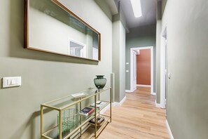 Un couloir avec un miroir, une console sur laquelle sont posés des livres et un vase.