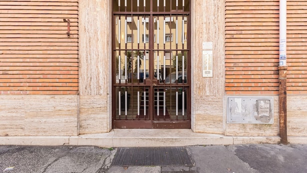 Une entrée d’immeuble avec un portail en métal, le numéro « 393 » au-dessus de la porte et une petite pancarte sur le mur.