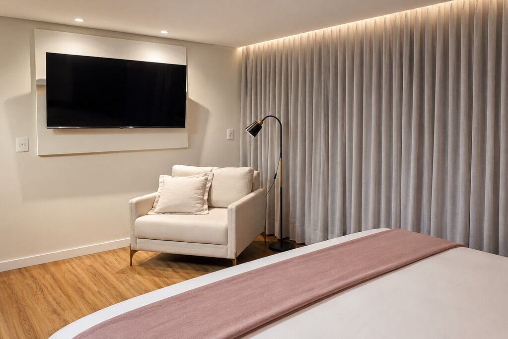 A hotel room with a bed, a sofa, a television mounted on the wall, and a floor lamp.