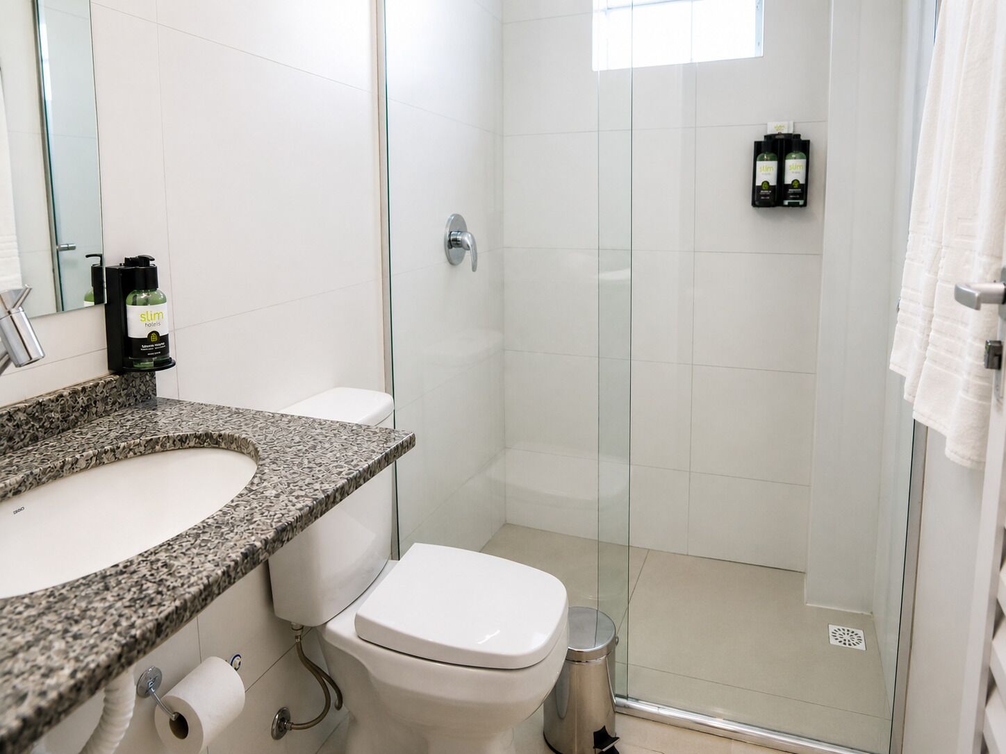 A bathroom with a granite countertop, a white toilet, a glass shower enclosure, and a towel rack.