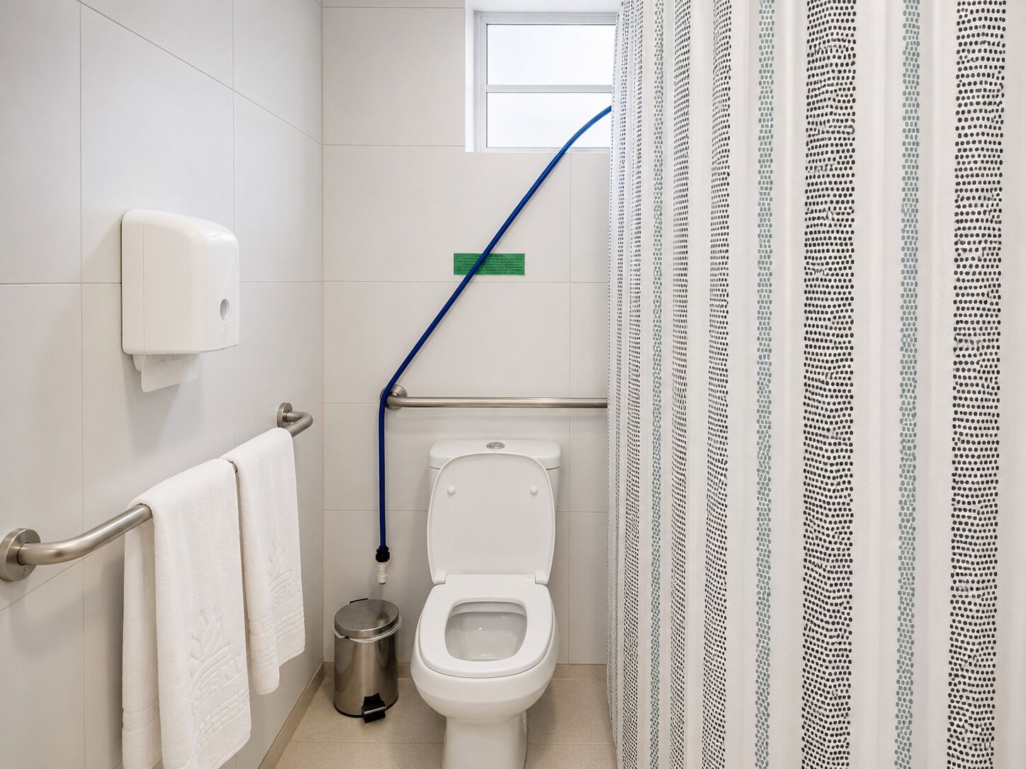 Ein Badezimmer mit Toilette, Handtrockner, Mülleimer, Haltegriff und Fenster.