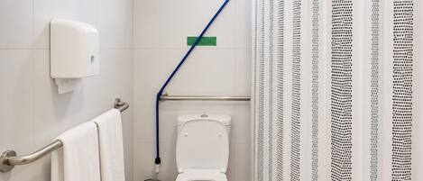 Ein Badezimmer mit Toilette, Handtrockner, Mülleimer, Haltegriff und Fenster.