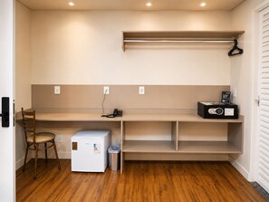 A compact kitchenette with a refrigerator, a coffee maker, a trash bin, and a chair.