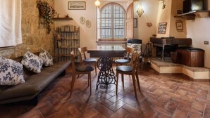 Ein rustikales Interieur mit Steinwand, Holzbalken, einem Esstisch mit Stühlen, einer Couch und einem Fernseher.