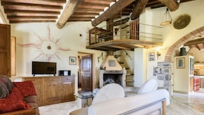 Ein rustikales Interieur mit Kamin aus Stein, Holzbalken, einer Couch und einem Fernseher.