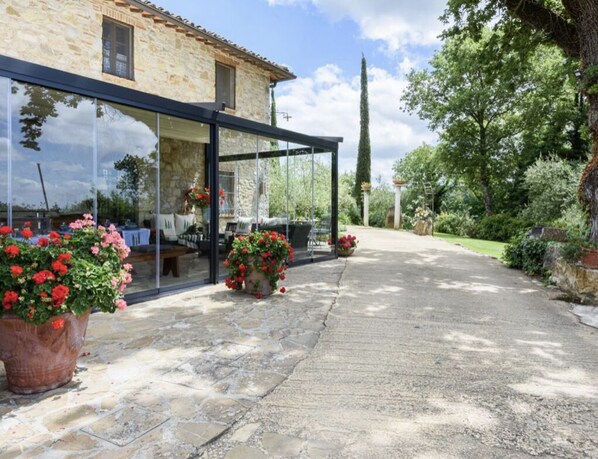 Un edificio in pietra con vetrate, vasi con fiori rossi e un sentiero in pietra che conduce a un giardino.