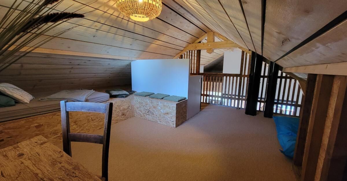 Un dormitorio abrigado en un ático con techo de madera, un banco de piedra, una silla y una cama con almohadas.