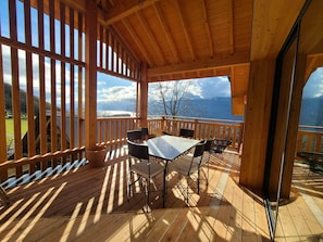 A wooden deck with a table and chairs, overlooking a mountainous landscape.