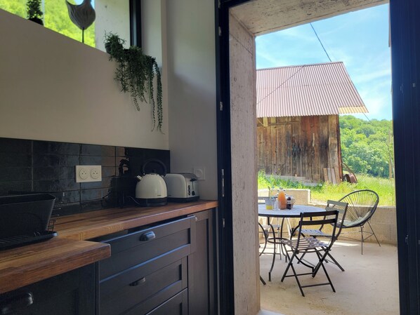 A kitchen with a laptop, kettle, and toaster on the counter. There is a dining area with a table and chairs outside. - L'Alpage (Brison-Saint-Innocent)