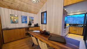 A modern kitchen with wooden cabinets, a dining area with a wooden table and chairs, and a view of the outdoors through a window. - L'Alpage (Brison-Saint-Innocent)