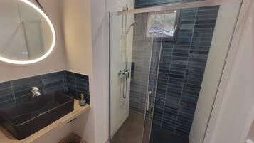 A modern bathroom with a glass-enclosed shower, a black sink, and a mirror with a circular light.
