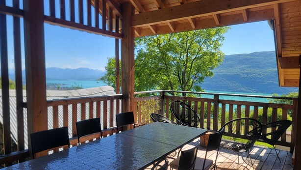 A covered outdoor area with a table and chairs, overlooking a scenic view of a lake and mountains. - L'Alpage (Brison-Saint-Innocent)