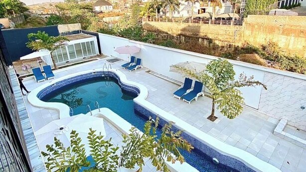 Una piscina sul tetto dalla forma particolare, circondata da poltrone a sdraio e ombrelloni, con vista su edifici residenziali e aree verdi.