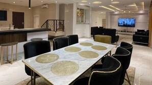 Zona pranzo moderna con tavolo in marmo, sedie nere e una televisione sullo sfondo.