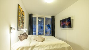 A neatly made bed with a remote control on a side table, a TV on the wall, and a painting on the wall. - Apartment Bad Gastein Near Ski Lift (Bad Gastein)