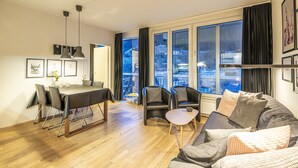 A modern living room with a dining area, large windows with curtains, and a view of the cityscape. - Apartment Bad Gastein Near Ski Lift (Bad Gastein)