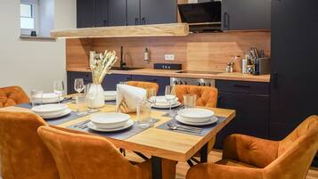 A modern kitchen with dark cabinets, a wooden countertop, and a dining area with orange chairs and a wooden table set for four.