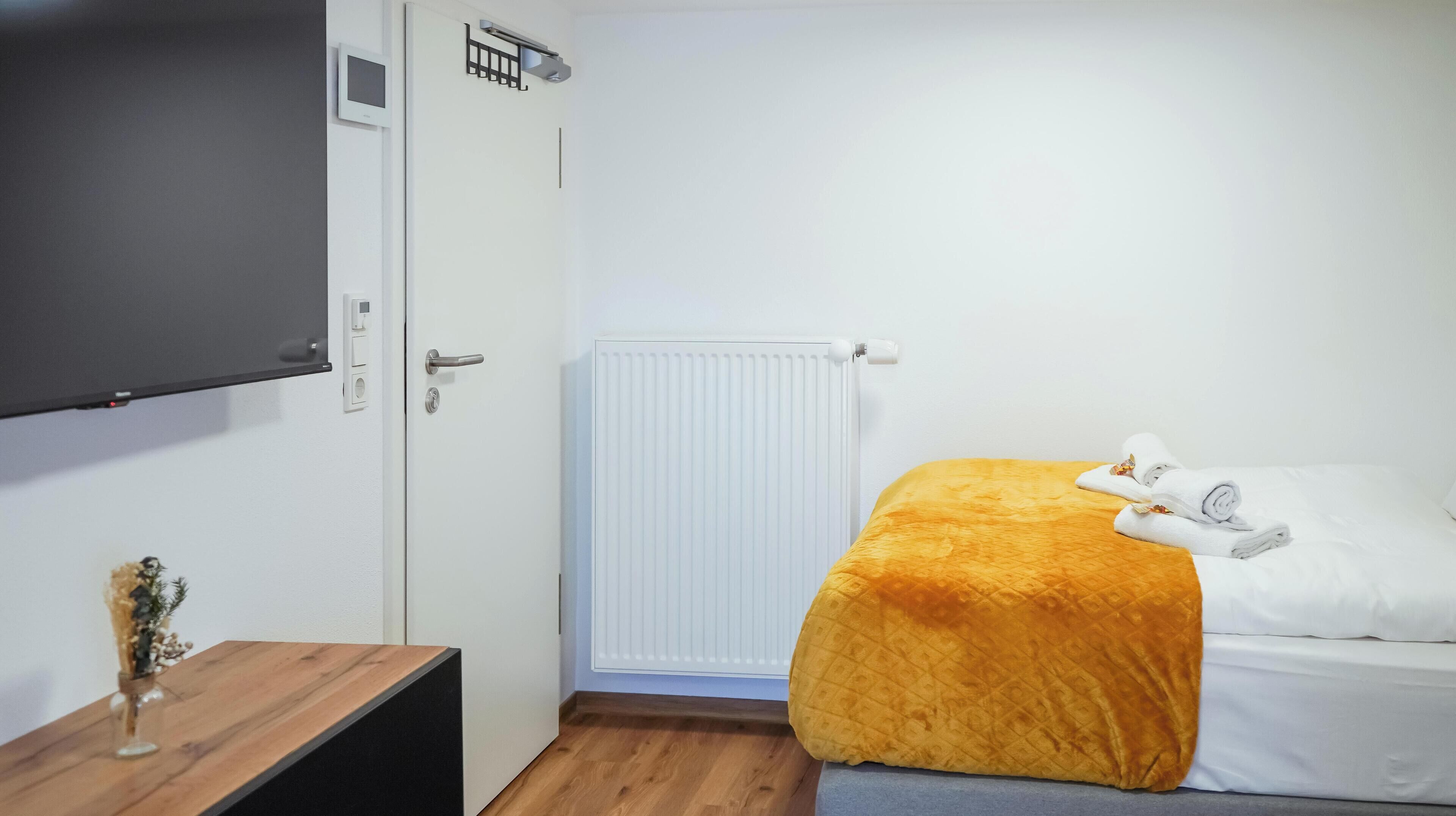 Una habitación de hotel con una cama, una mesita de noche de madera, un radiador blanco y un televisor montado en la pared.
