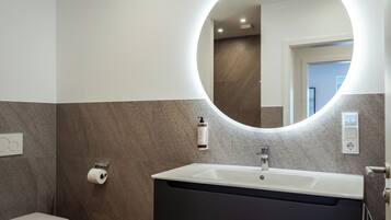 A bathroom with a white sink, dark vanity, and a round mirror with built-in lighting.