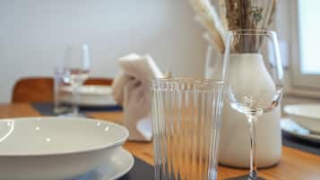 A dining table with a white plate, a clear glass, and a vase with dried plants.