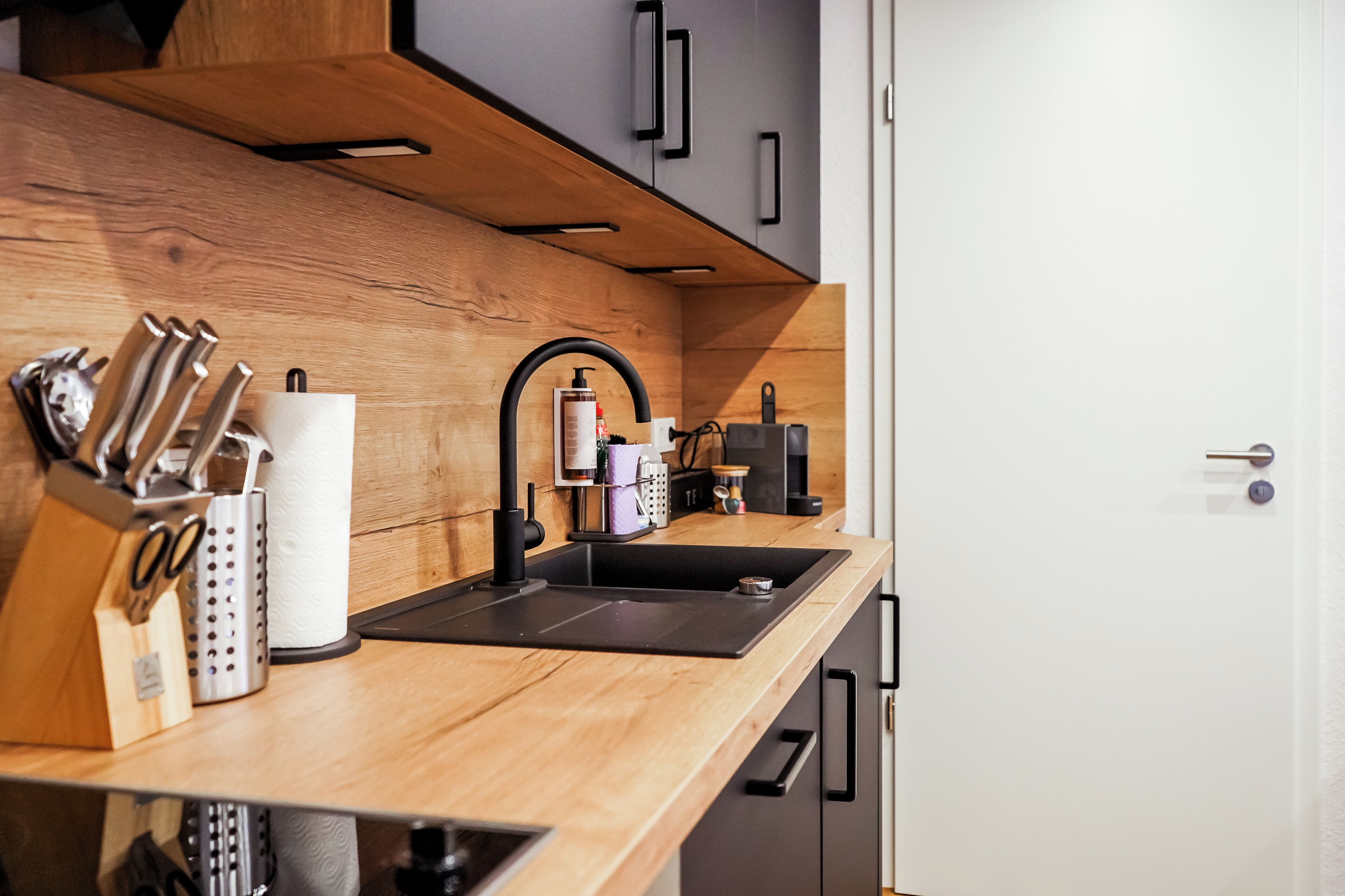 A modern kitchen with a wooden countertop, black sink, and stainless steel appliances.