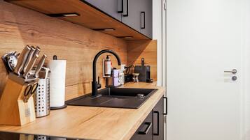 A modern kitchen with a wooden countertop, black sink, and stainless steel appliances.