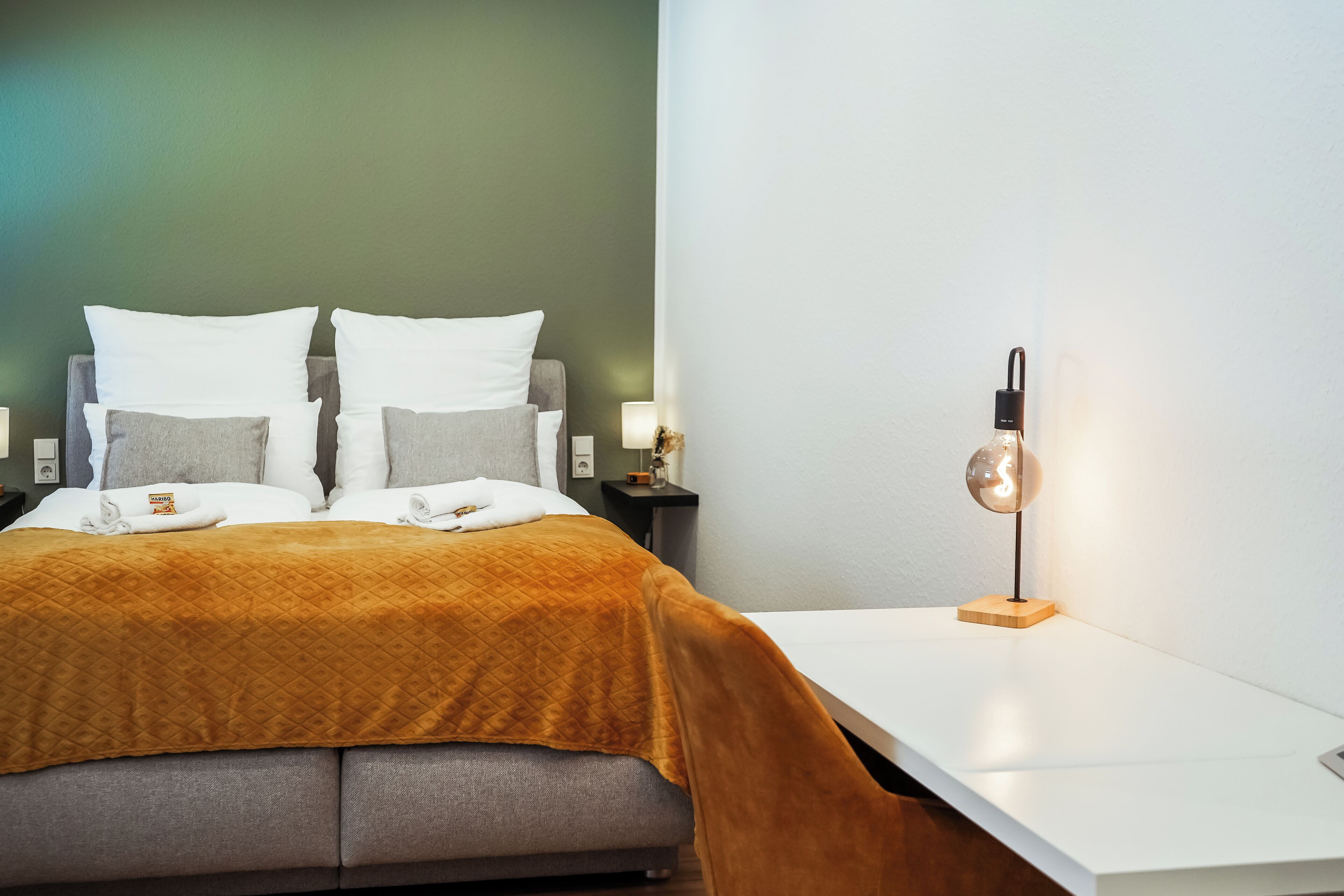 A neatly made bed with a quilted blanket, a bedside table with a lamp, and a wall-mounted light fixture.