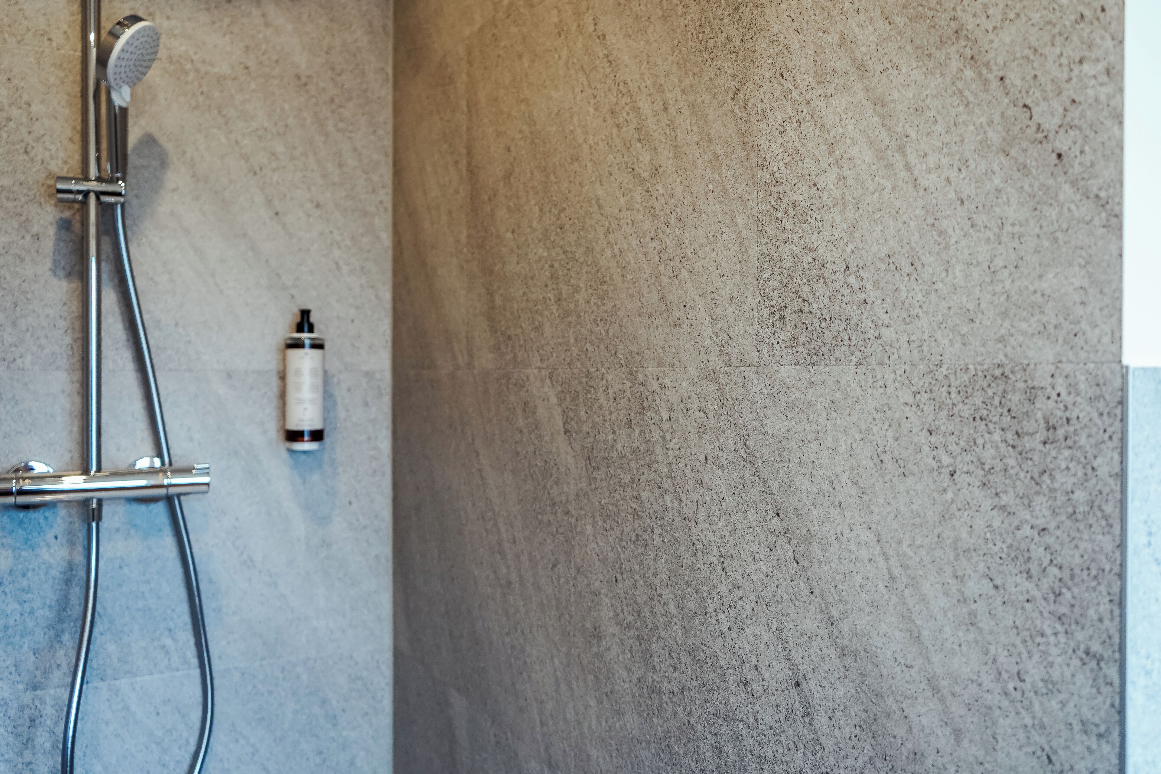 Zona de ducha con cabezal de ducha de mano y una botella de champú en la pared.