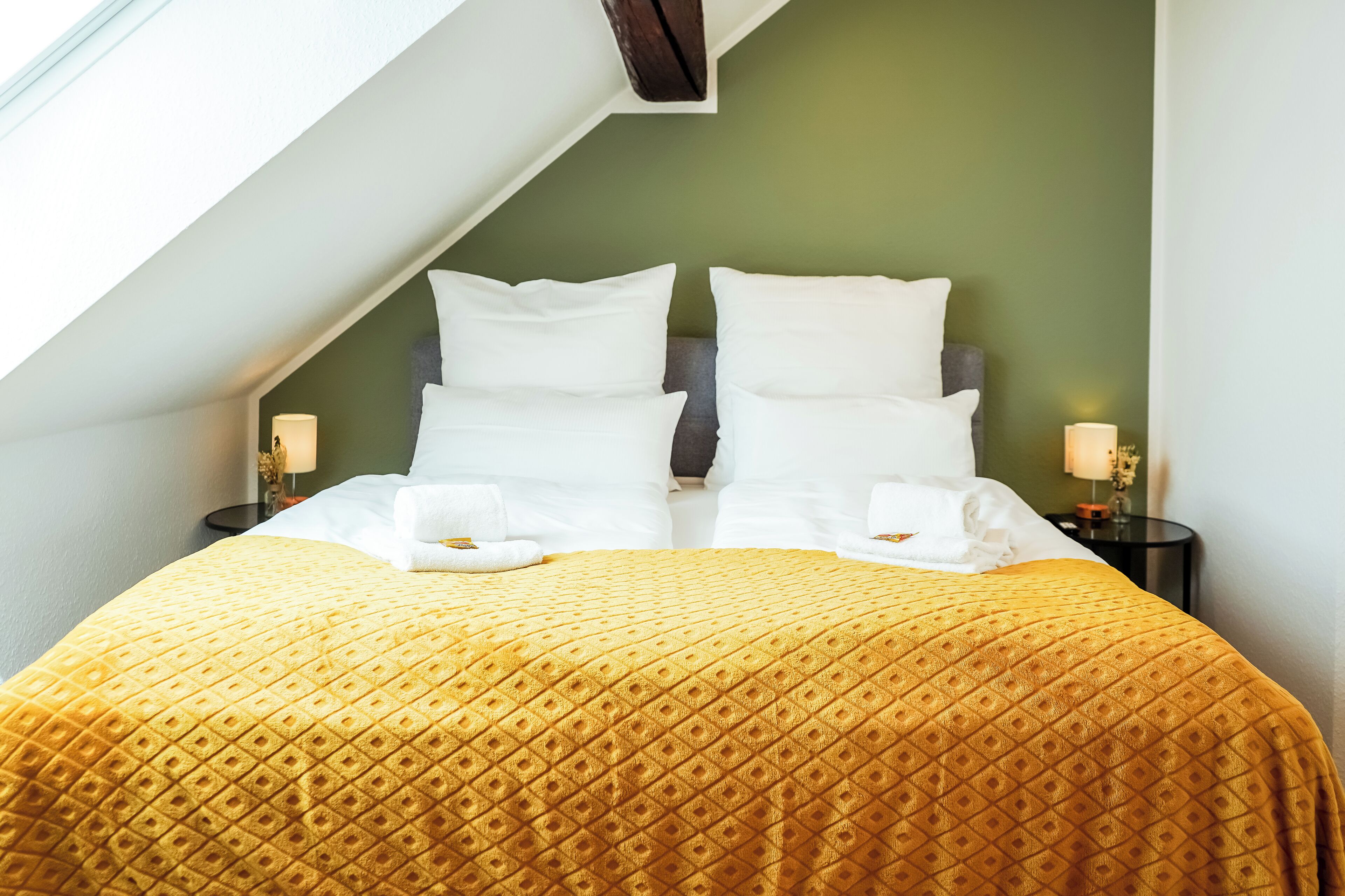 A room with a bed, two nightstands, and a skylight.