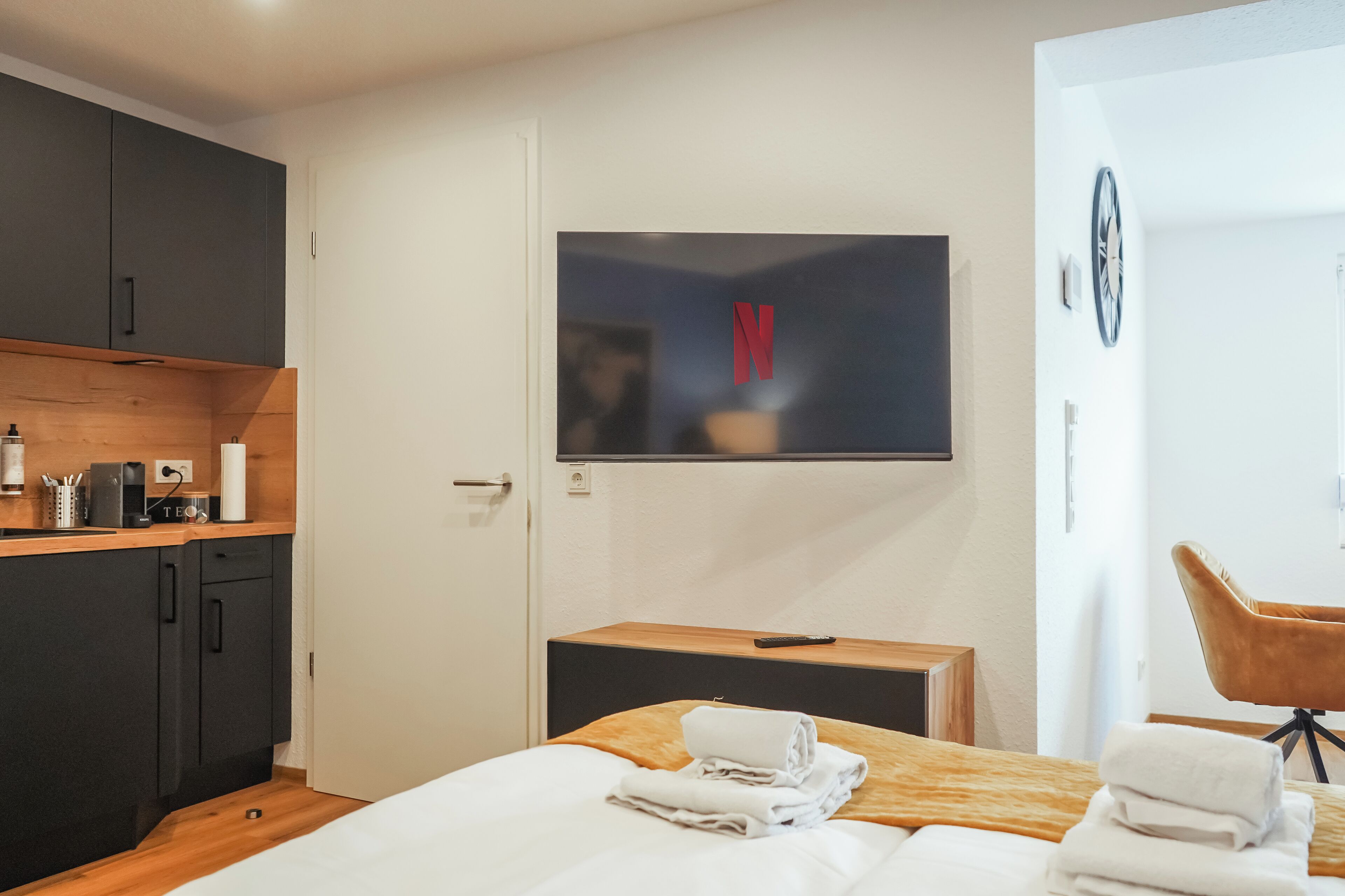 Ein Hotelzimmer mit Bett, Wandfernseher, Schreibtisch aus Holz, Stuhl und Kleiderschrank.
