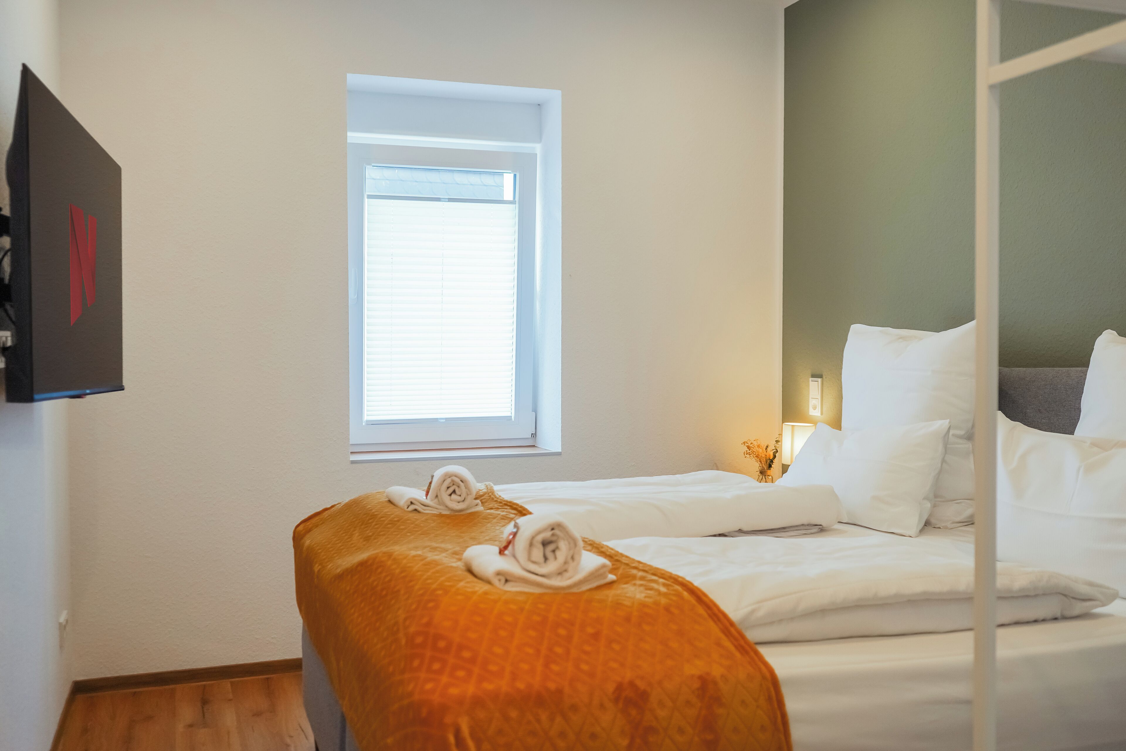 A hotel room with a bed, a window, and a bench with towels.