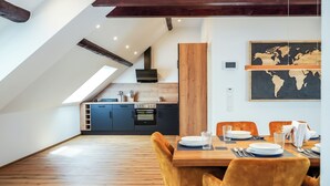 Ein stilvoller Essbereich mit einem Holztisch und Samtstühlen, im Hintergrund eine Küche und eine Weltkarte an der Wand.