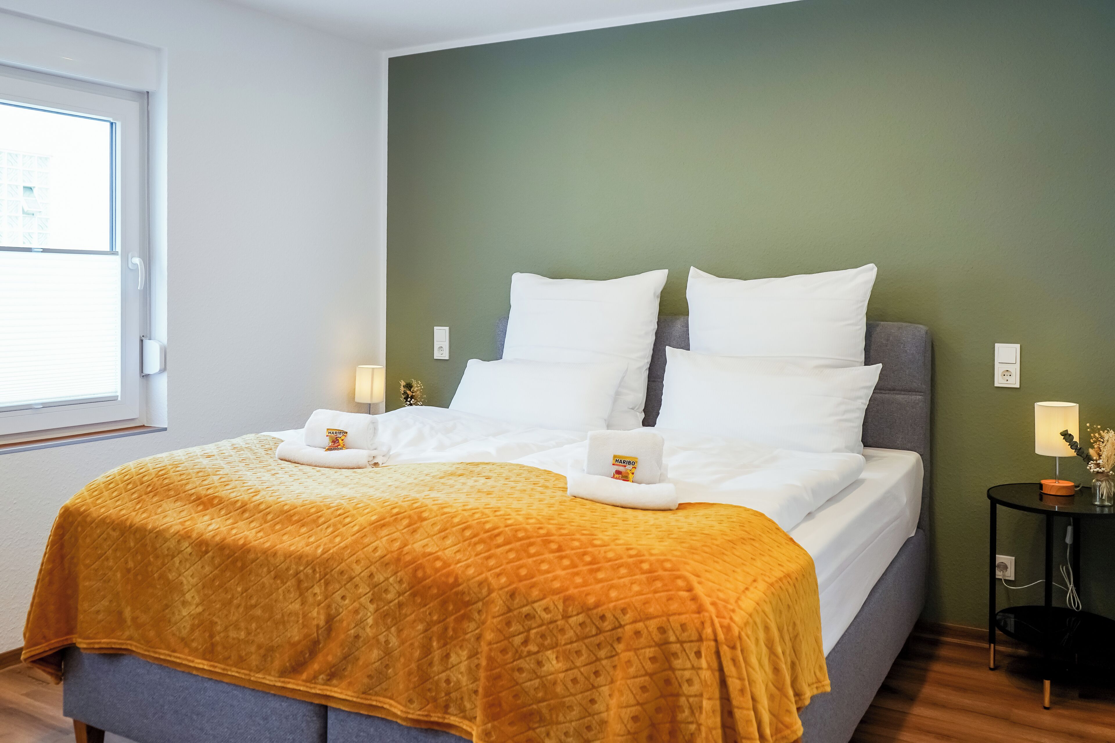A neatly made bed with a patterned blanket, pillows, and a small towel with a logo.