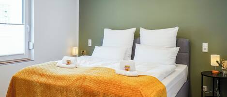 A neatly made bed with a patterned blanket, pillows, and a small towel with a logo.