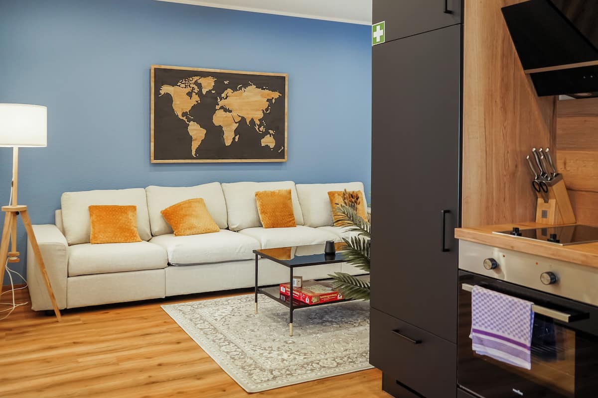 A living room with a sofa, a coffee table, a world map on the wall, and a kitchen area with a stove and oven.