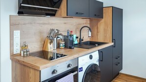 Eine kompakte Küche mit Holztischplatte, integriertem Backofen, Waschmaschine und grauen Schränken.